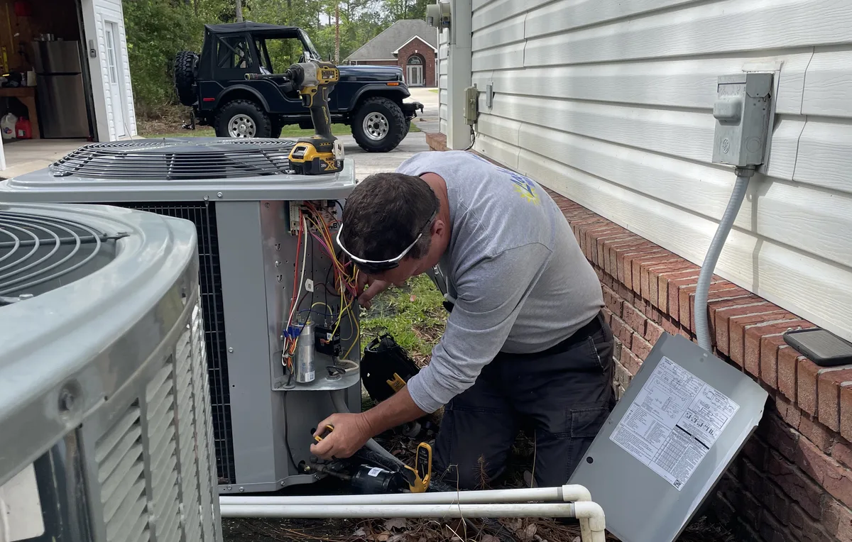 Lake Area Heating & Air technician working inside an outdoor AC condenser beside a Keystone Heights home