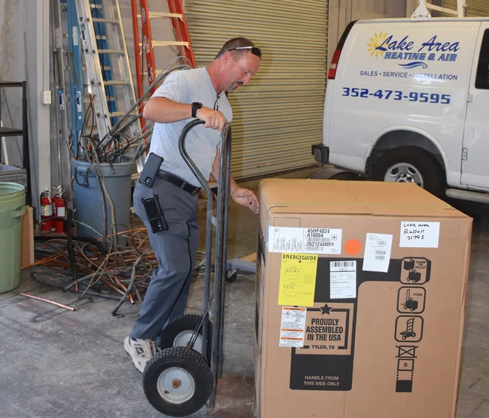 Lake Area Heating & Air technician wheeling a new boxed central AC system out of the shop