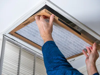 Technician replacing a whole-home air filter in a ceiling return vent